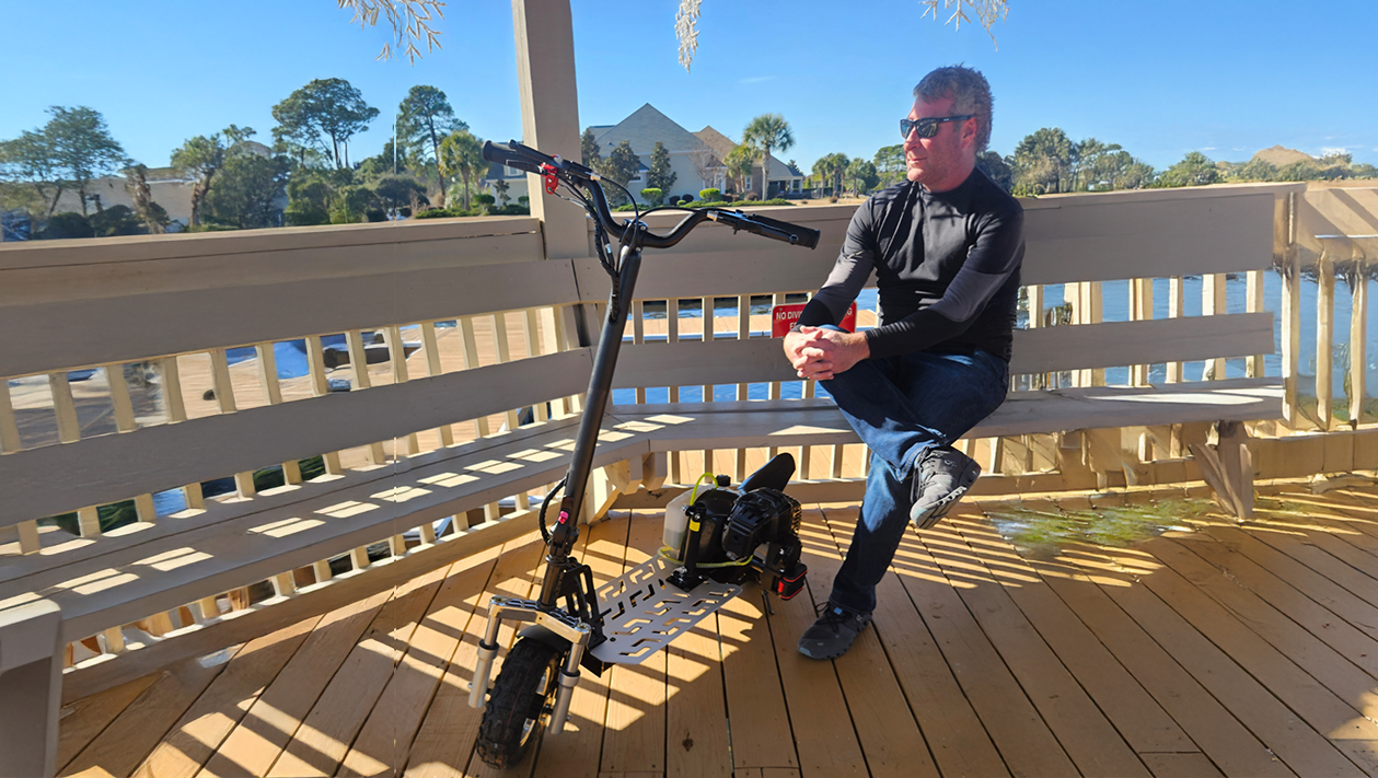 Scooter with a 6′ tall man sitting next to it on a bench